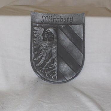 Metallisches Wappen von Nürnberg mit einem Adler und diagonal gestreiftem Feld in Schwarz und Silber.