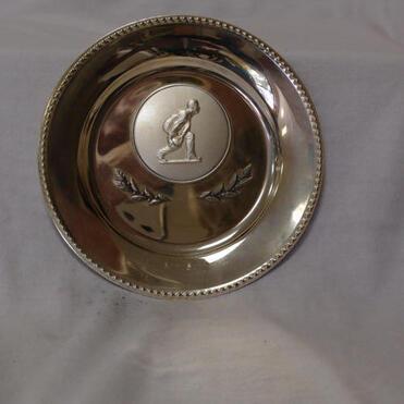 Silberne Medaille mit erhabenem Sportler-Relief und Laubornamenten auf einem weißen Hintergrund.