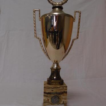 Großer goldfarbener Pokal mit verziertem Griff auf einem marmorierten Sockel, vor einem weißen Hintergrund.