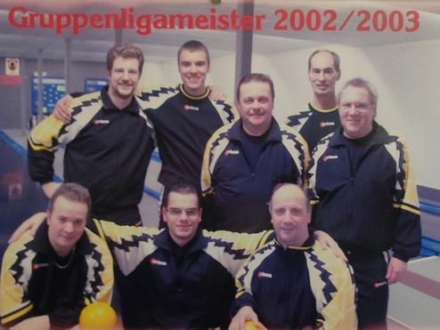 Gruppe von acht Bowlingspielern in schwarzen und gelben Jacken, posieren l&auml;chelnd vor einer Bowlingbahn.