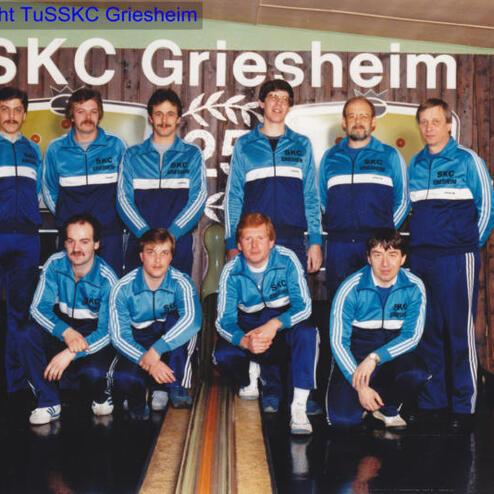 Gruppenaufnahme von neun Männern in blauen Sportanzügen, vor einer Kegelbahn mit dem Schriftzug „SKC Griesheim“.