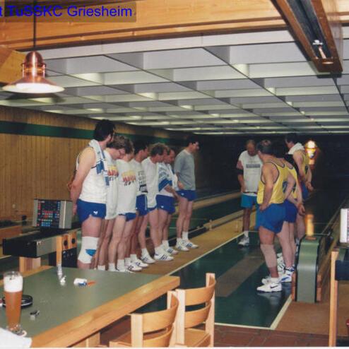 Gruppe von Sportlern in Freizeitkleidung steht an einer Kegelbahn, im Hintergrund eine Kegelbahn mit Geräten.