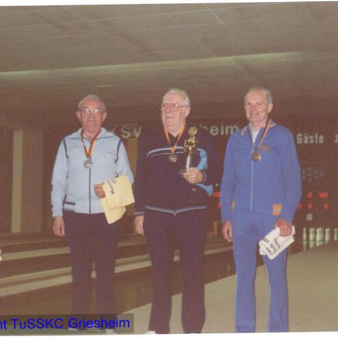 Vier Medaillenträger stehen beim Kegel-Event auf dem Podium, während Zuschauer im Hintergrund applaudieren.
