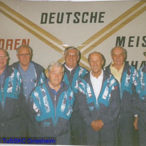 Gruppenfoto von sechs Männern in Sportjacken vor einer Wand mit der Aufschrift „Deutsche Senioren Meisterschaften“.
