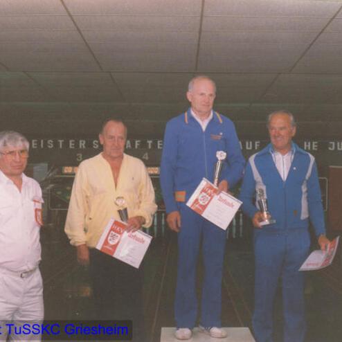 Vier Männer stehen auf einem Podest, halten Pokale und Urkunden in einer Kegelhalle.
