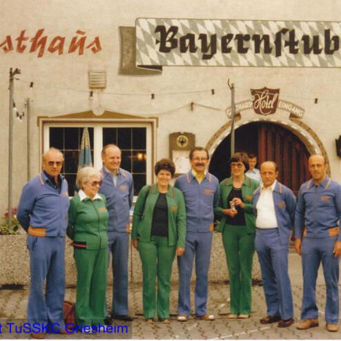 Gruppenfoto von acht Personen in Arbeitskleidung vor dem Gasthaus "Bayernstuben" mit sichtbarem Eingang und Dekoration.