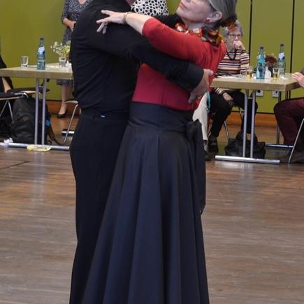Tanzpaar in eleganter Kleidung beim Tango, umgeben von Zuschauern in einem festlichen Raum.