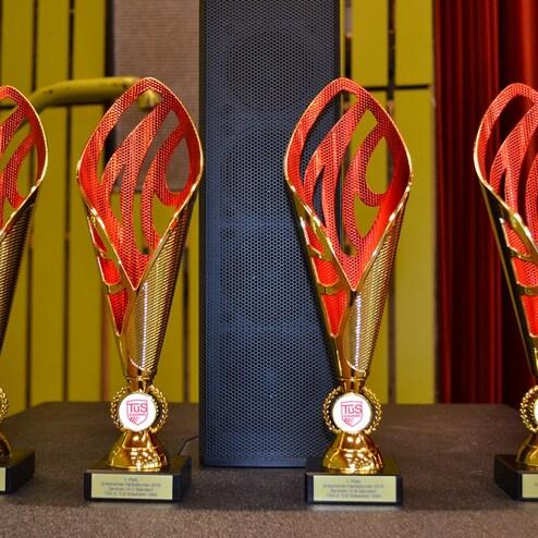 Vier Pokale mit rot-goldenem Design auf einem Tisch, platziert vor einem schwarzen Lautsprecher.