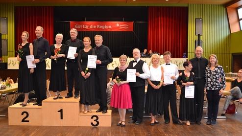Teilnehmer eines Tanzwettbewerbs stehen auf einem Siegerpodium mit Urkunden und Blumen in der Hand.