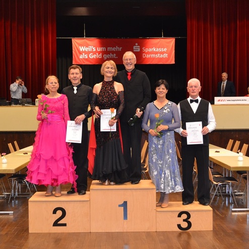 Sechs tanzende Paare auf dem Treppchen, jeweils mit Urkunden, in festlicher Kleidung bei einer Veranstaltung.