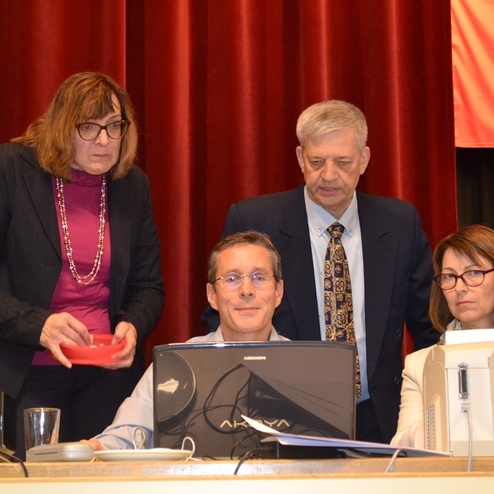 Vier Personen stehen um einen Computer an einem Tisch in einem Konferenzraum, w&auml;hrend sie sich auf den Bildschirm konzentrieren.