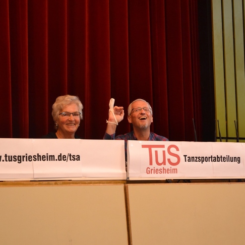 Zwei l&auml;chelnde Personen stehen am Tisch mit einem Schild der Tanzsportabteilung von TuS Griesheim.