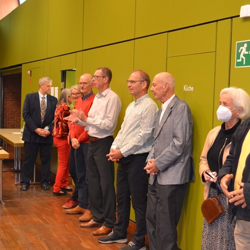 Gruppe von Personen in der Warteschlange vor einer gr&uuml;nen Wand, einige tragen Mund-Nasen-Schutzmasken.