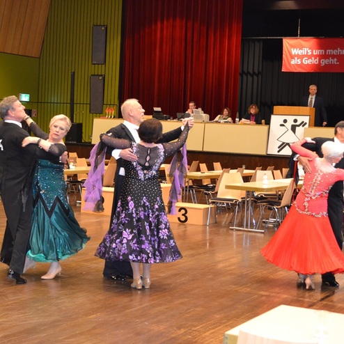 Tanzpaaren in eleganter Ballkleidung bei einem Wettbewerb in einer festlich dekorierten Halle.