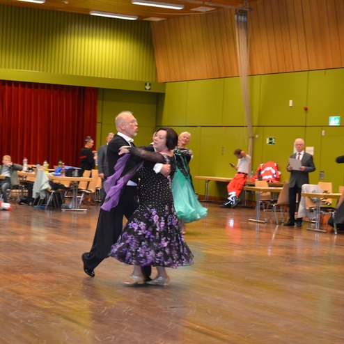 Tanzende Paare in eleganter Kleidung auf einer Tanzfl&auml;che mit Zuschauern in einem beleuchteten Saal.