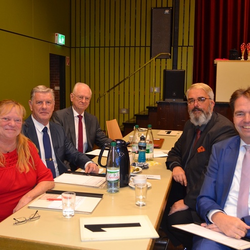 F&uuml;nf Personen sitzen an einem Tisch, umgeben von Getr&auml;nken und Unterlagen in einem Veranstaltungsraum.