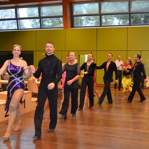 Tanzpaare in festlicher Kleidung gehen in einer Halle in einer Reihe, um ihre Choreografie zu pr&auml;sentieren.