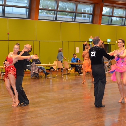 Zwei Paare tanzen leidenschaftlich in Schmuckkost&uuml;men auf einem Parkettboden in einer Turnierumgebung.