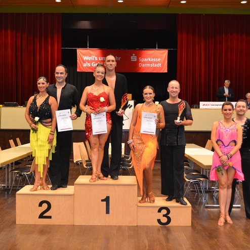 Sieben T&auml;nzer stehen auf dem Siegertreppchen bei einem Tanzwettbewerb, jeder mit Urkunde in der Hand.