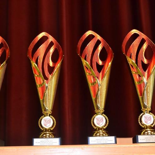 Vier Pokale mit rotem und goldenem Design, auf einem Regal vor einem roten Vorhang.