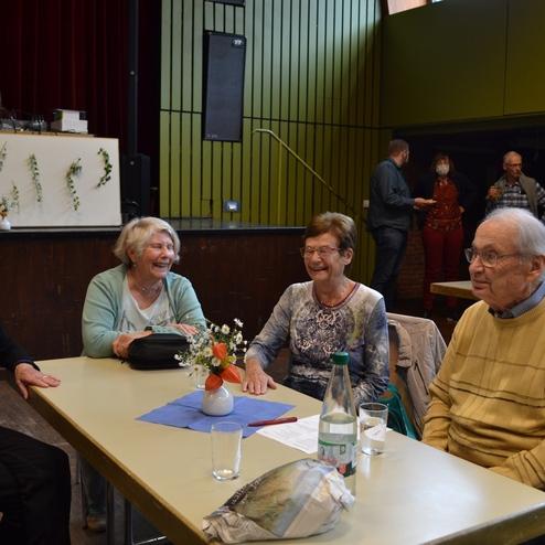 Vier &auml;ltere Menschen sitzen an einem Tisch, l&auml;cheln und unterhalten sich in einem festlich dekorierten Raum.