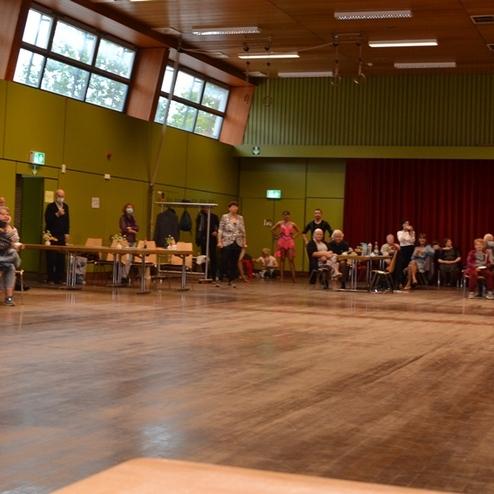 Tanzende Paare in festlicher Kleidung auf einer Tanzfl&auml;che, Zuschauer sitzen an Tischen im Hintergrund.