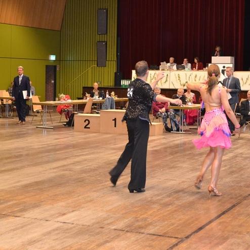 Tanzpaare in auff&auml;lligen Kost&uuml;men tanzen auf einer Tanzfl&auml;che vor einer Jury und Publikum bei einem Wettbewerb.