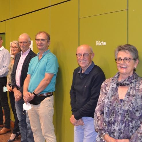 Sechs Personen stehen l&auml;chelnd an einer gr&uuml;nen Wand, die den Zugang zur K&uuml;che zeigt, in einem Innenraum.