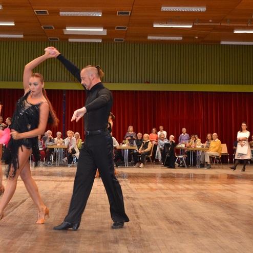 Tanzpaar in festlicher Kleidung auf einer Tanzfl&auml;che, Zuschauer im Hintergrund sitzen an Tischen.