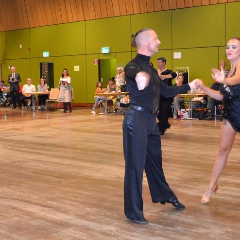 Tanzpaare zeigen einen leidenschaftlichen Tanzwettbewerb auf einer Holzfl&auml;che in einem festlichen Raum.