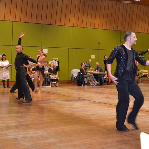 Tanzpaar im Wettbewerb, elegant gekleidet, auf einer Holzbodenfl&auml;che mit Zuschauern im Hintergrund.