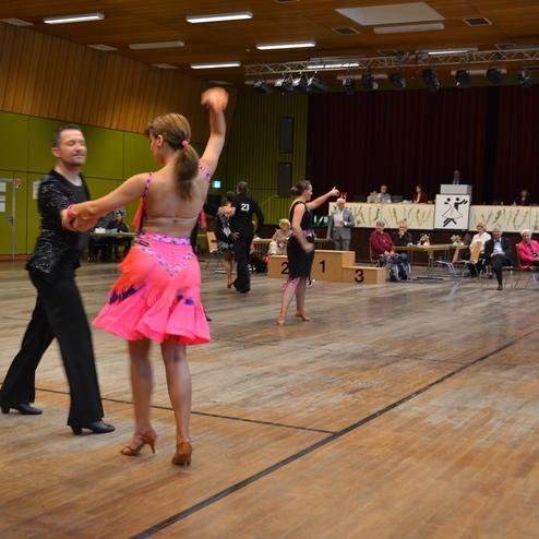 Tanzpaar in eleganter Kleidung tritt bei einem Wettbewerb in einer Halle auf, w&auml;hrend Zuschauer aufmerksam beobachten.