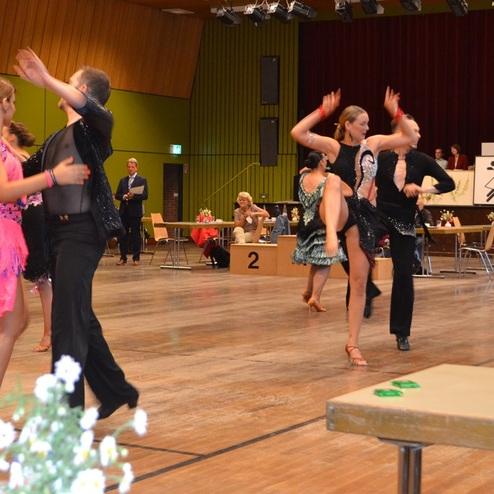 Tanzgruppe in eleganter Kleidung f&uuml;hrt Paartanz auf einer Wettbewerbsfl&auml;che vor Publikum vor.