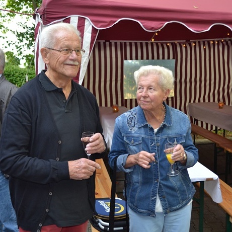 Paar älterer Menschen stehen an einem festlich dekorierten Tisch, trinken Sekt und unterhalten sich.