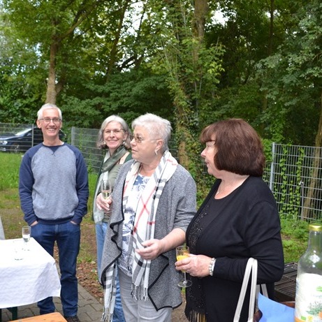 Gruppe von fünf Menschen steht in einer natürlichen Umgebung und unterhält sich bei einem geselligen Beisammensein.