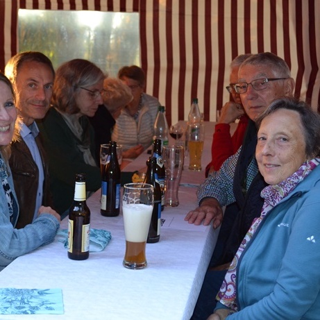 Sechs Personen sitzen an einem Tisch im Zelt, Getränke stehen vor ihnen, im Hintergrund weitere Gäste.