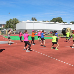 Gruppe von Frauen in bunten T-Shirts, die auf einem Sportplatz gemeinsam Fitnessübungen machen.