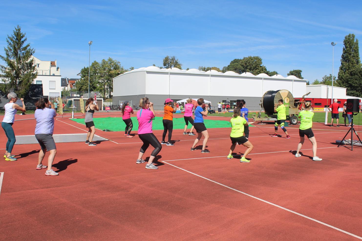 Gruppe von Frauen in bunten T-Shirts, die auf einem Sportplatz gemeinsam Fitnessübungen machen.