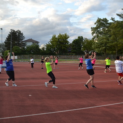 Gruppe von Sportlern in bunten T-Shirts auf einem roten Platz beim Üben von Bewegungen unter freiem Himmel.
