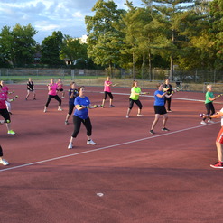 Gruppe von Frauen in Sportbekleidung führt ein Workout mit Gewichten auf einem Tennisplatz durch.