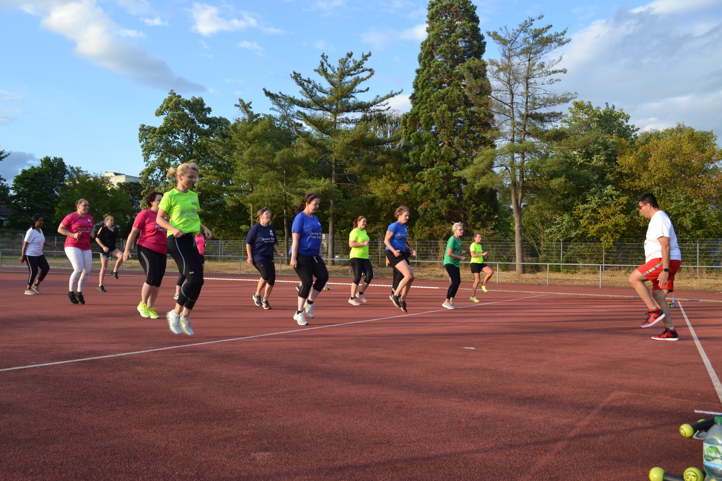 Gruppe von Frauen in Sportkleidung trainiert auf einem roten Sportplatz unter blauem Himmel.