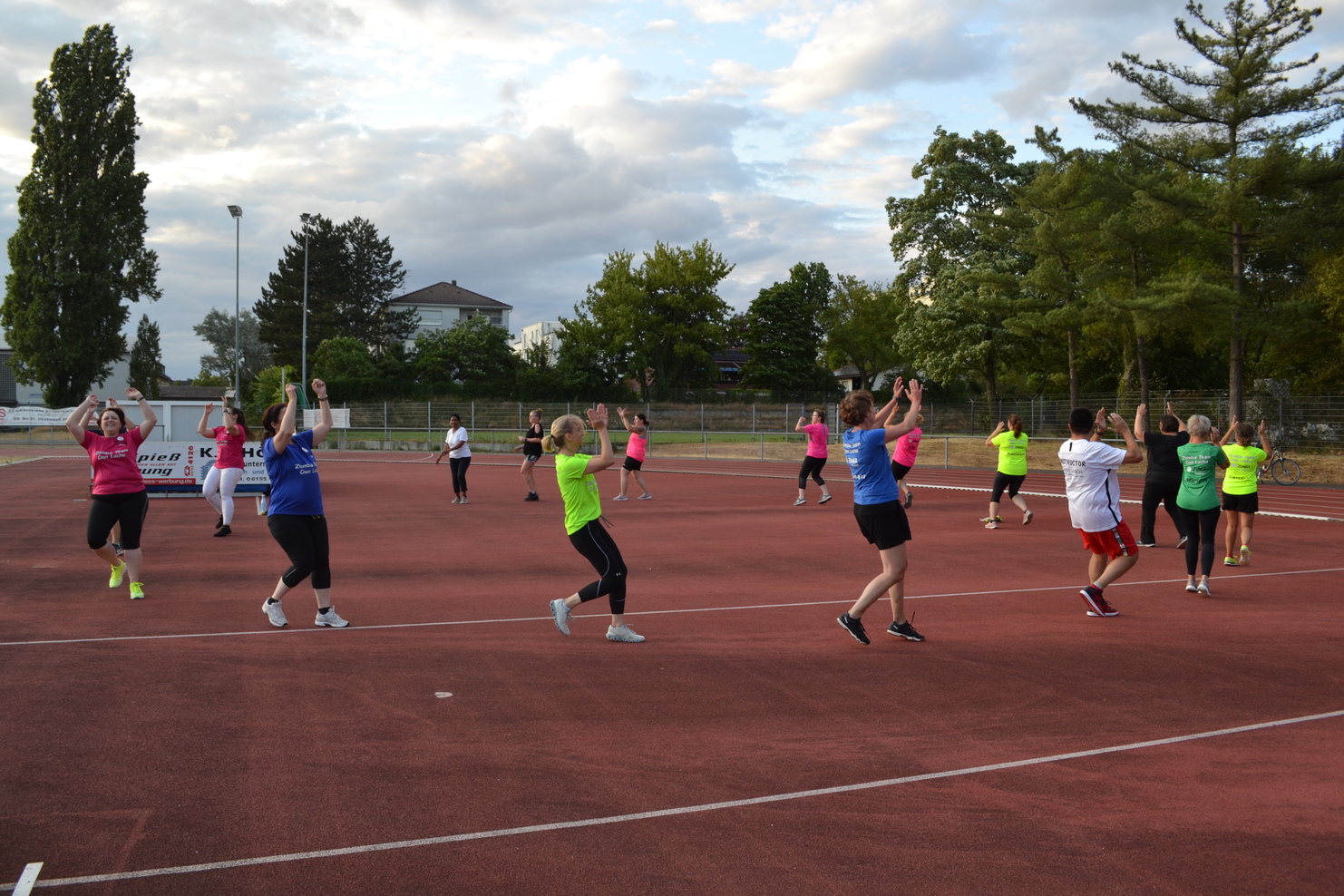 Gruppe von Sportlern in bunten T-Shirts auf einem roten Platz beim Üben von Bewegungen unter freiem Himmel.