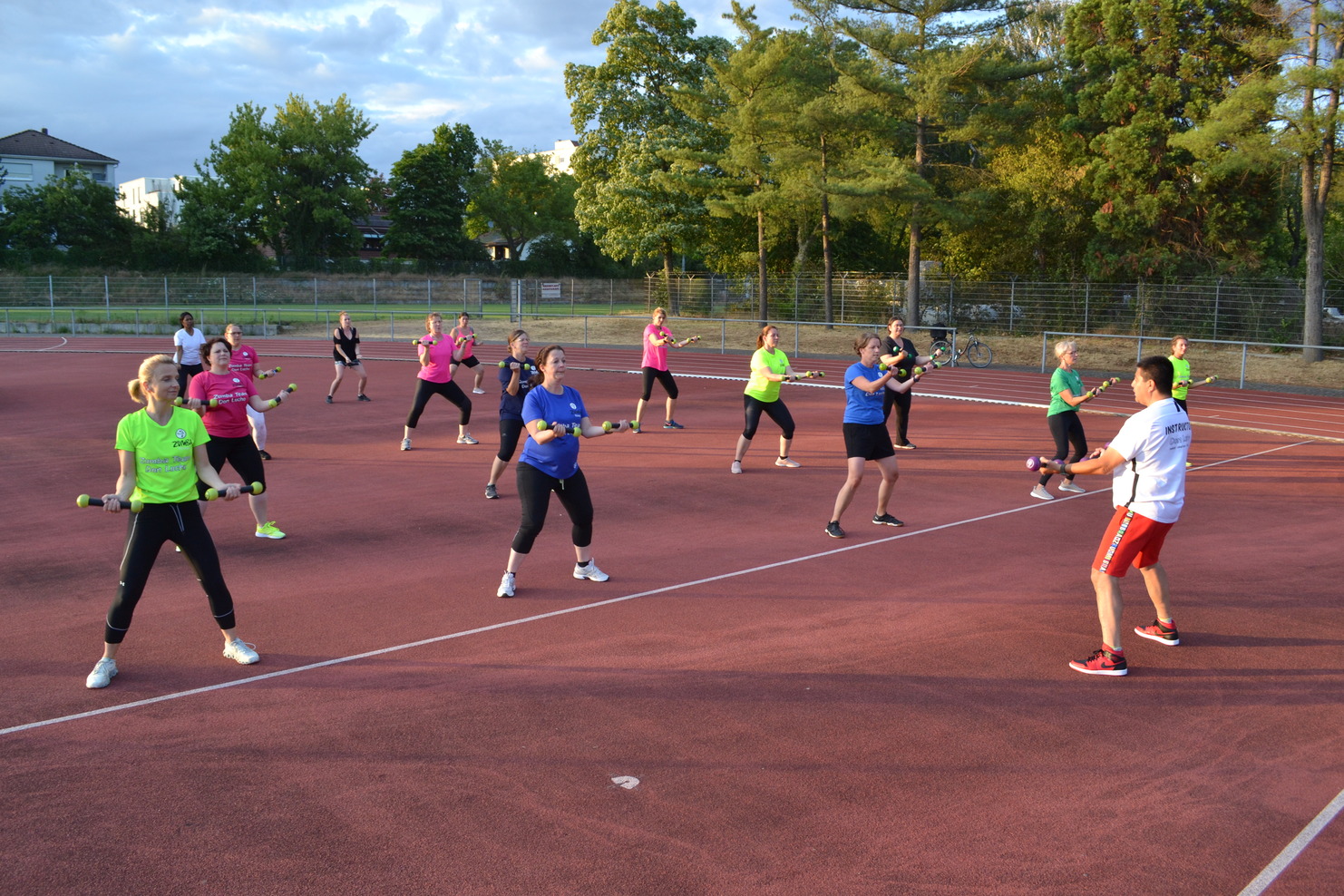 Gruppe von Frauen in Sportbekleidung führt ein Workout mit Gewichten auf einem Tennisplatz durch.