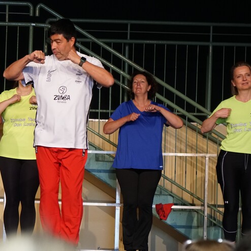 Zumba-Kurs mit einer Gruppe von vier Teilnehmern, die rhythmisch tanzen und einen Trainer in der Mitte unterstützen.