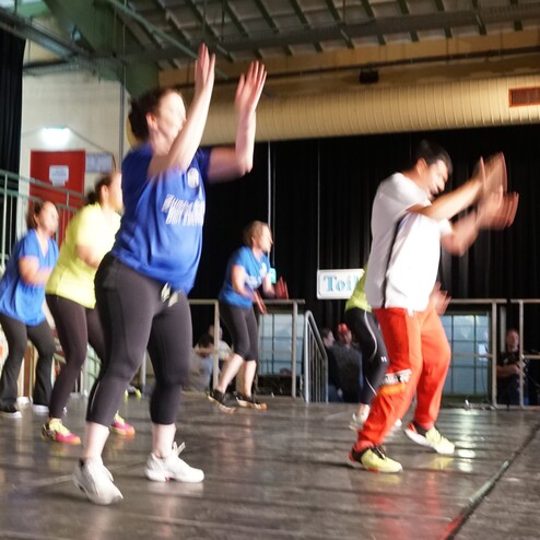 Gruppe von Menschen in Sportkleidung tanzt gemeinsam auf einer Bühne während einer Fitnessveranstaltung.