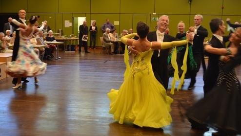 Tanzpaare in eleganter Kleidung tanzen auf einer Wettkampf-B&uuml;hne vor einem Publikum in einem festlichen Saal.