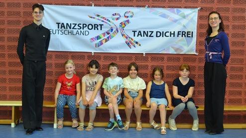 Gruppe von Kindern und zwei Erwachsenen vor einem Banner mit der Aufschrift &bdquo;Tanzsport Deutschland&ldquo;.