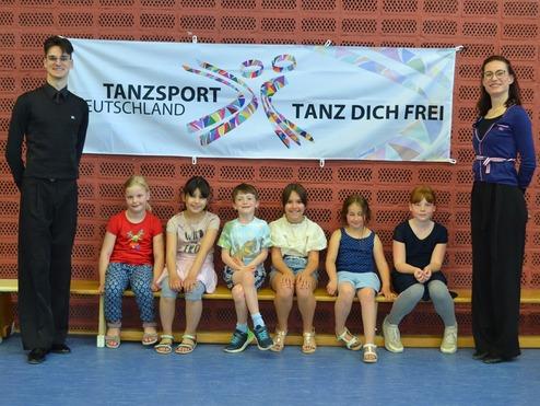 Gruppe von Kindern und zwei Erwachsenen vor einem Banner mit der Aufschrift „Tanzsport Deutschland“.