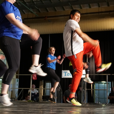 Gruppentanzauff&uuml;hrung mit Teilnehmern in Sportkleidung auf einer B&uuml;hne, Bewegung und Energie sichtbar.
