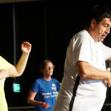 Vier Personen in Sportkleidung tanzen in einem lichtdurchfluteten Raum zu Zumba-Musik.